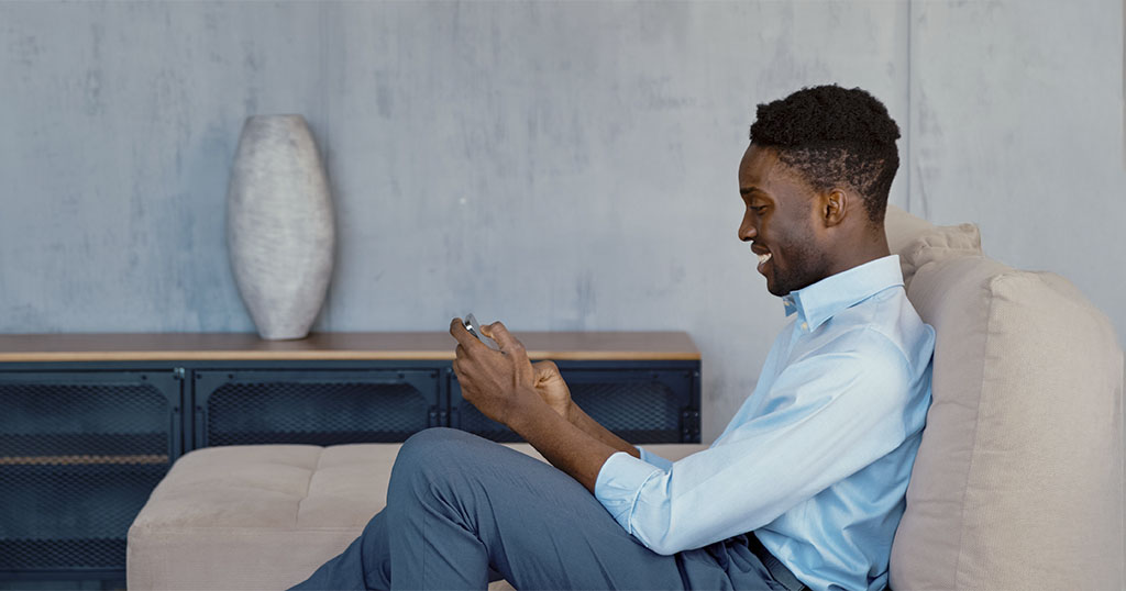 Un homme assis sur un canapé sourit en regardant son téléphone