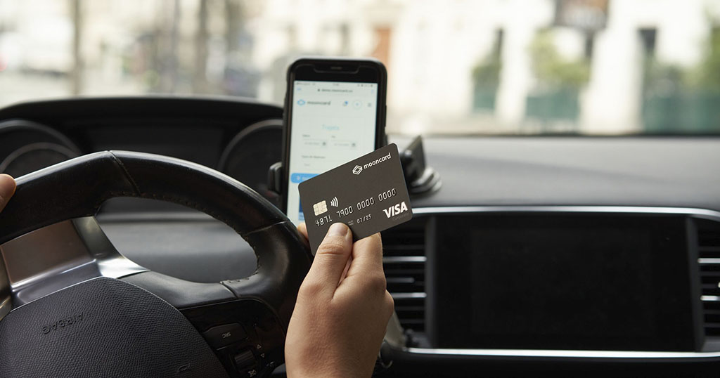 Une personne tient une carte de crédit dans une voiture, un téléphone est fixé au tableau de bord